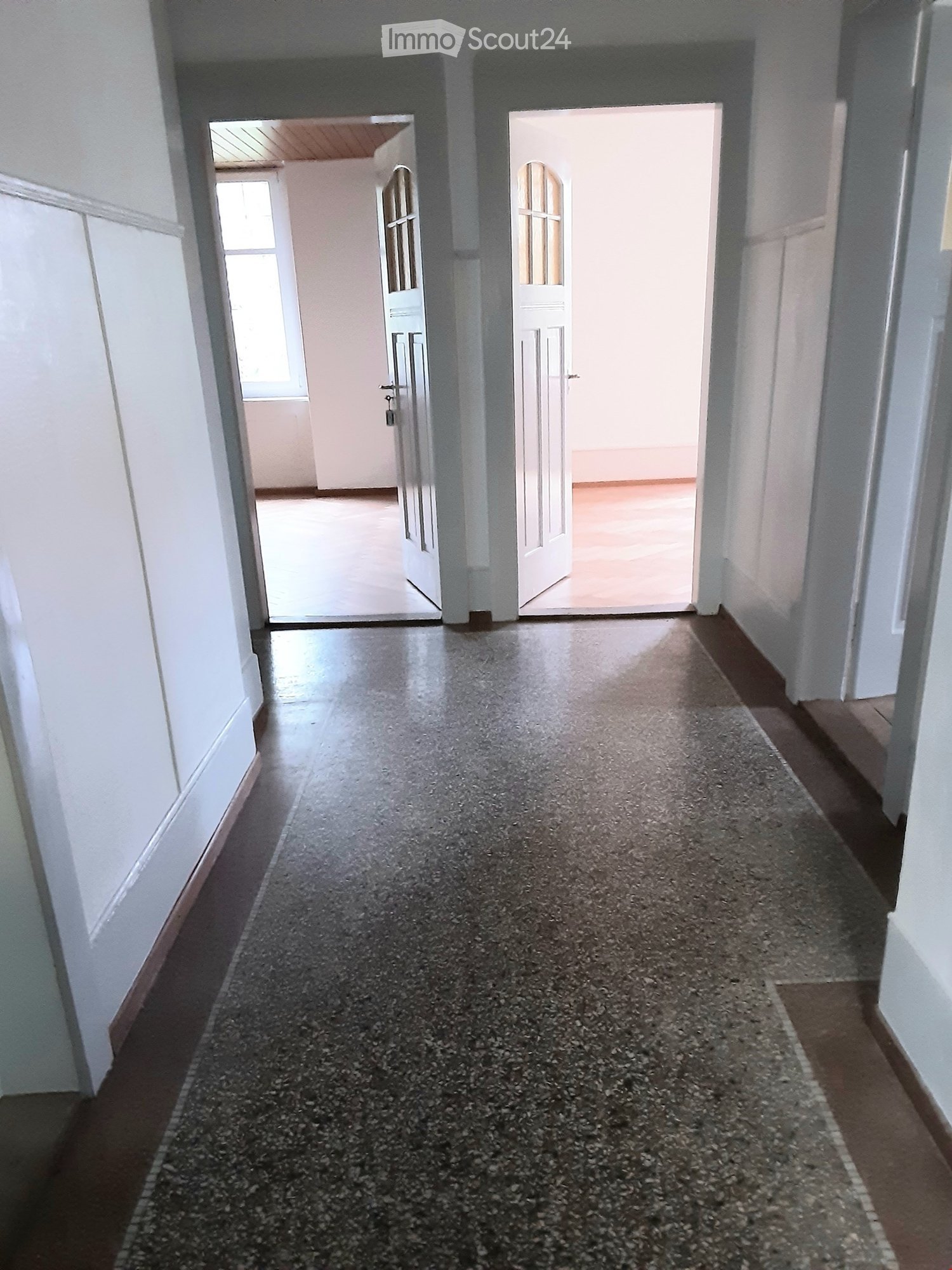 Empty hallway with white walls, gray speckled floor, and two open doors leading to other rooms.
