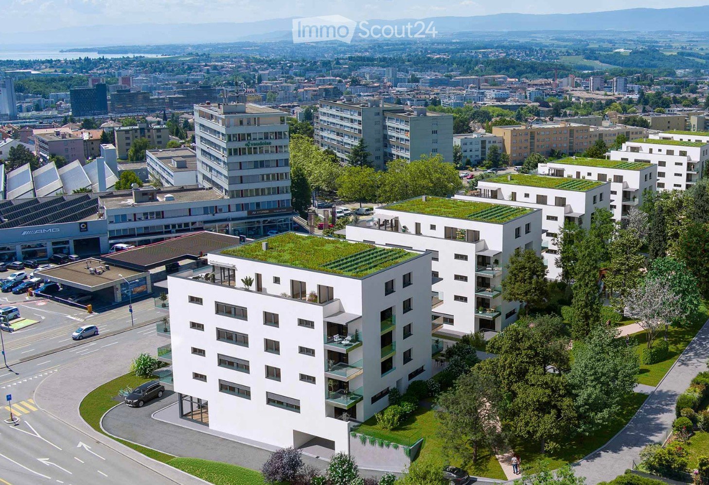 Aerial view of a modern urban residential complex with multiple white apartment buildings, green rooftop gardens, and surrounding infrastructure including parking lots, roads, and nearby commercial buildings.