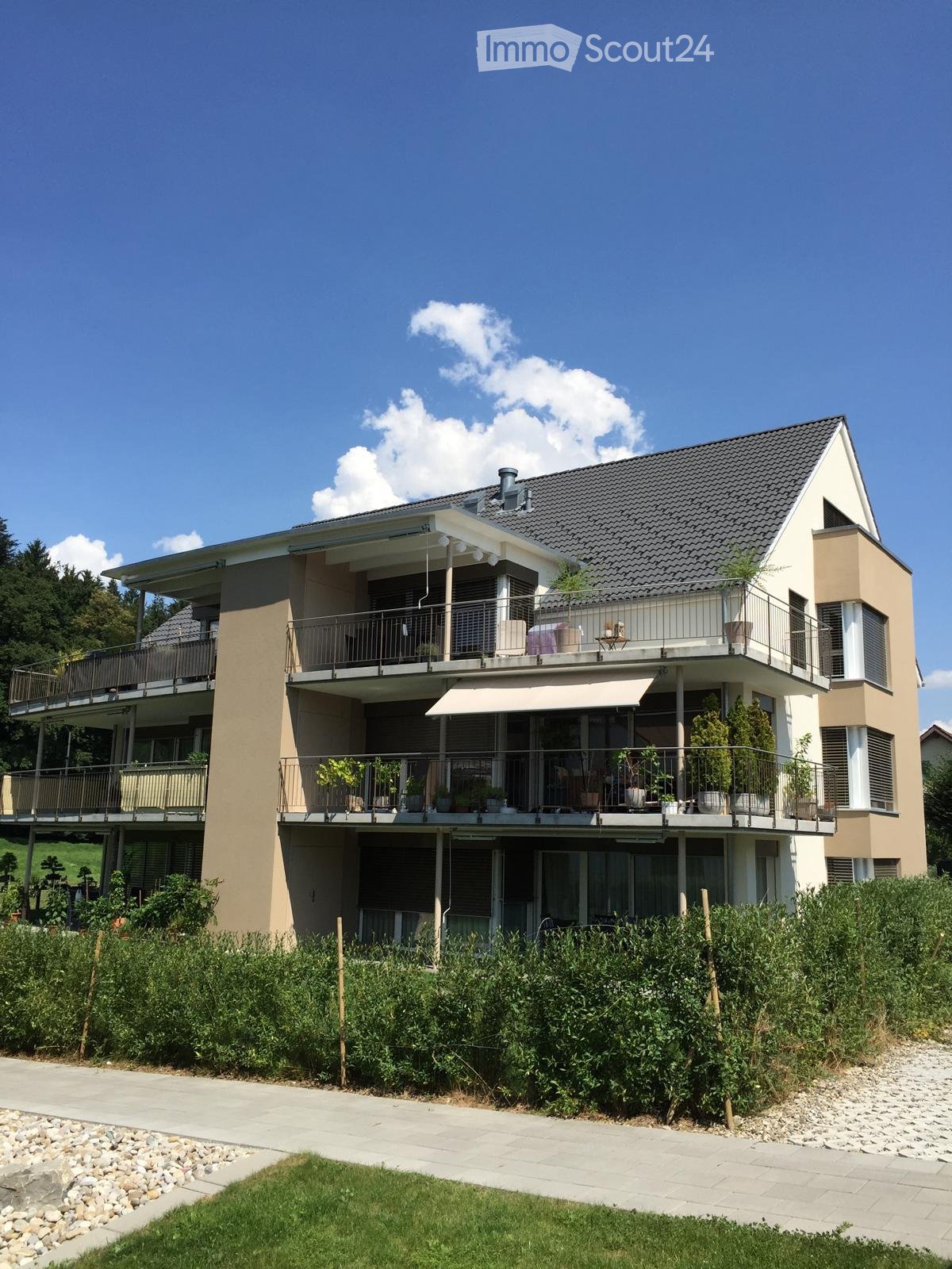 House. Modern two-story house with beige and white exterior, multiple balconies, large windows, and surrounding greenery.