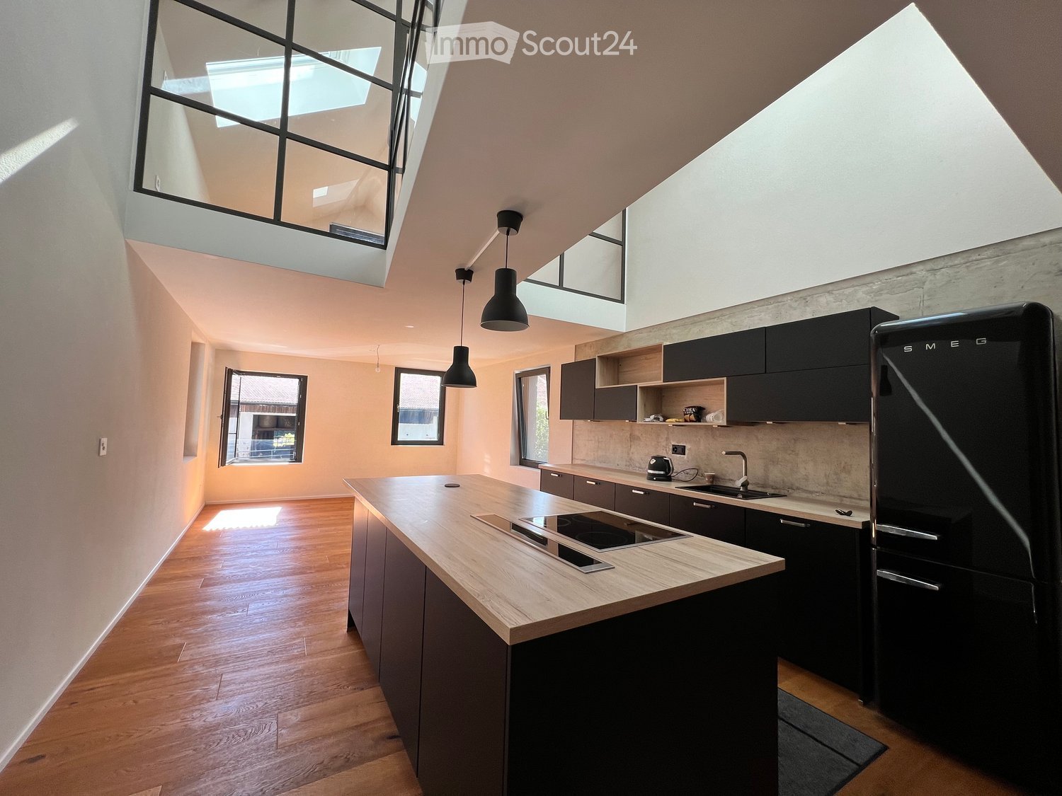 Modern kitchen with light wooden countertops, black cabinets, stainless steel appliances, and pendant lights.