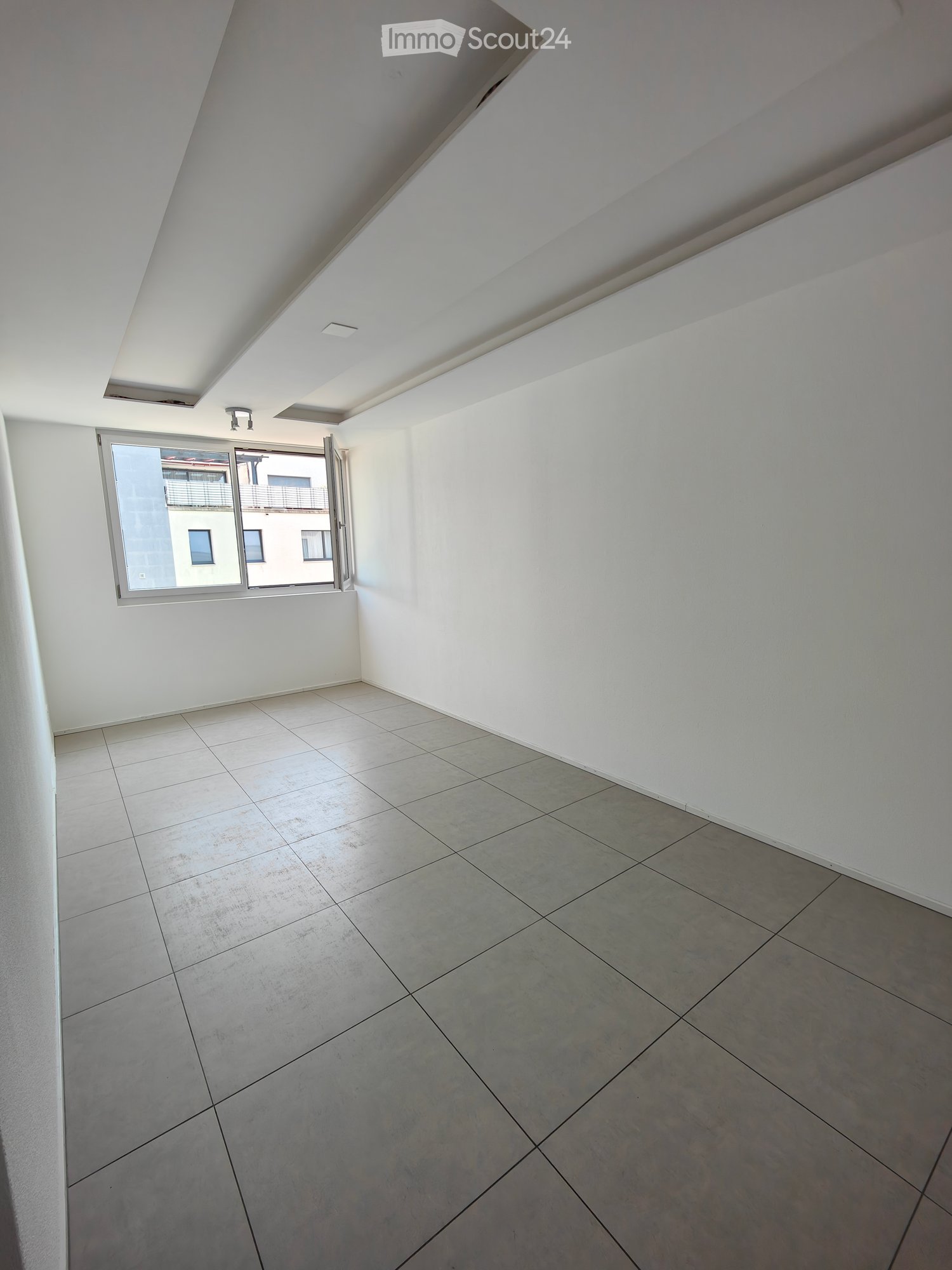 Empty room with white walls, tiled floor, and a large window with a view of another building.