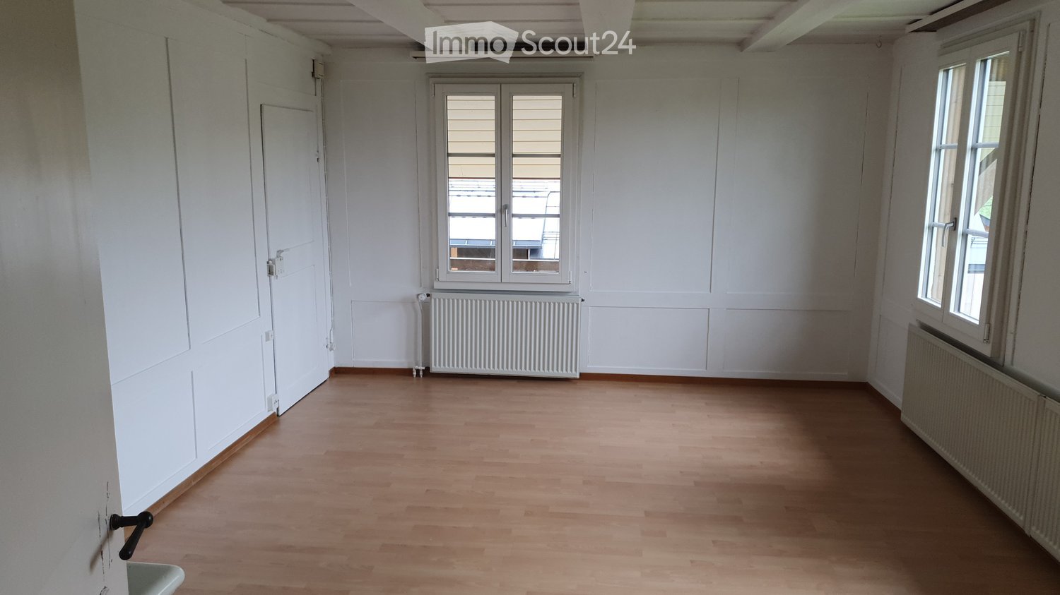 Empty room with wooden flooring, white walls, and two windows. Radiators are visible beneath the windows.