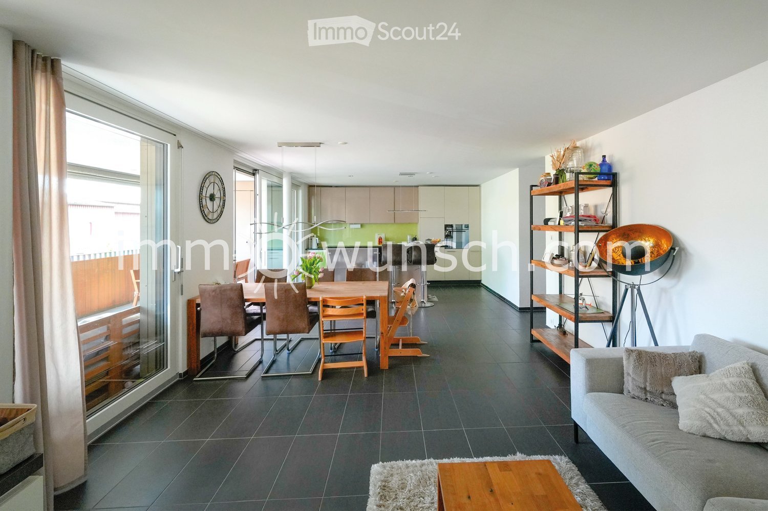 Modern living and dining area with a grey sofa, wooden coffee table, dining table with chairs, shelves, and decorative items.