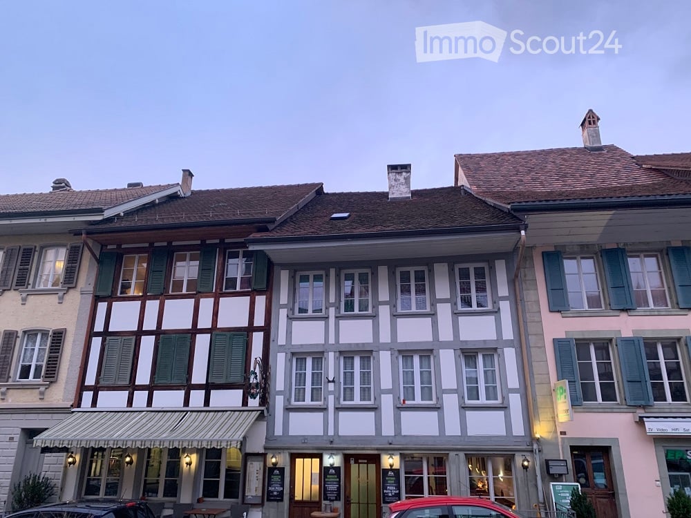 A row of traditional European townhouses with varied facades, including timber-framed and plaster designs, multiple windows, and awnings.