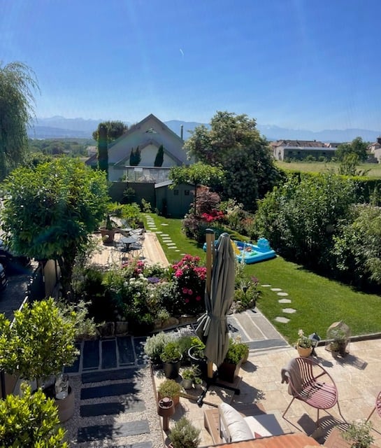 Well-maintained garden with a patio, outdoor furniture, potted plants, and a swimming pool in the background.
