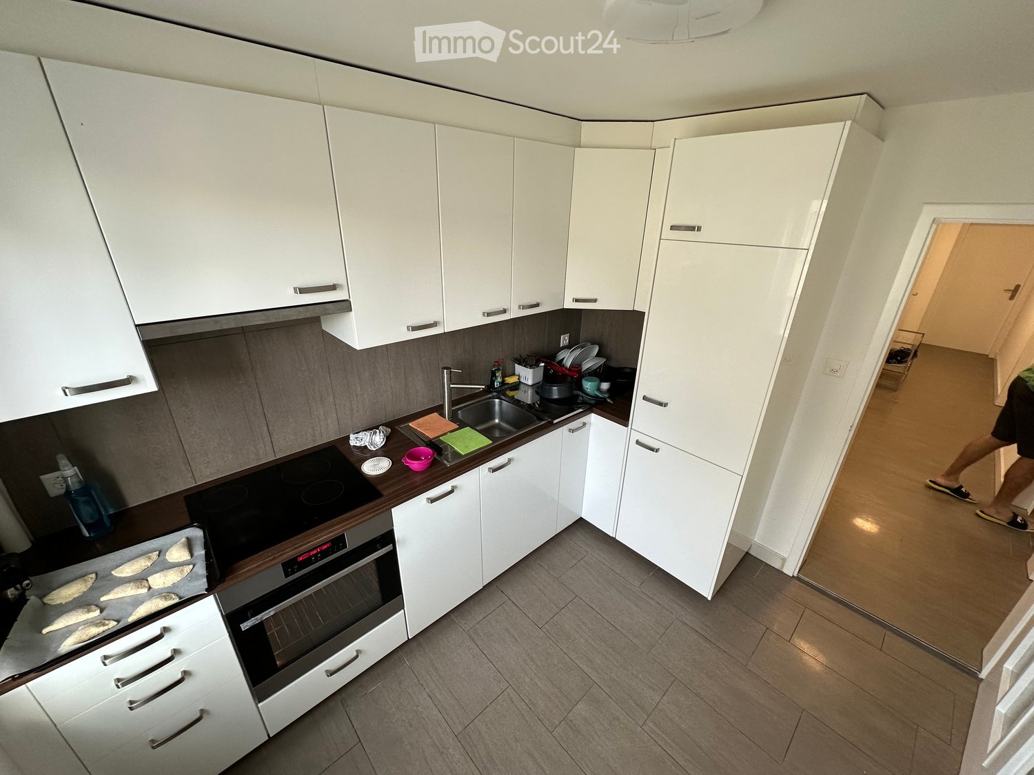 Modern kitchen with white cabinets, stainless steel appliances, and a wooden countertop. Visible items include an oven, sink, faucet, and oven tray with food.