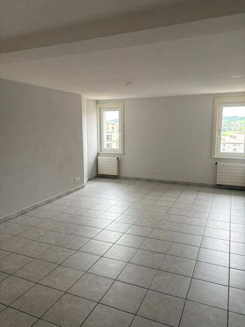 Empty room with tiled floor, white walls, and two windows with radiators beneath them.