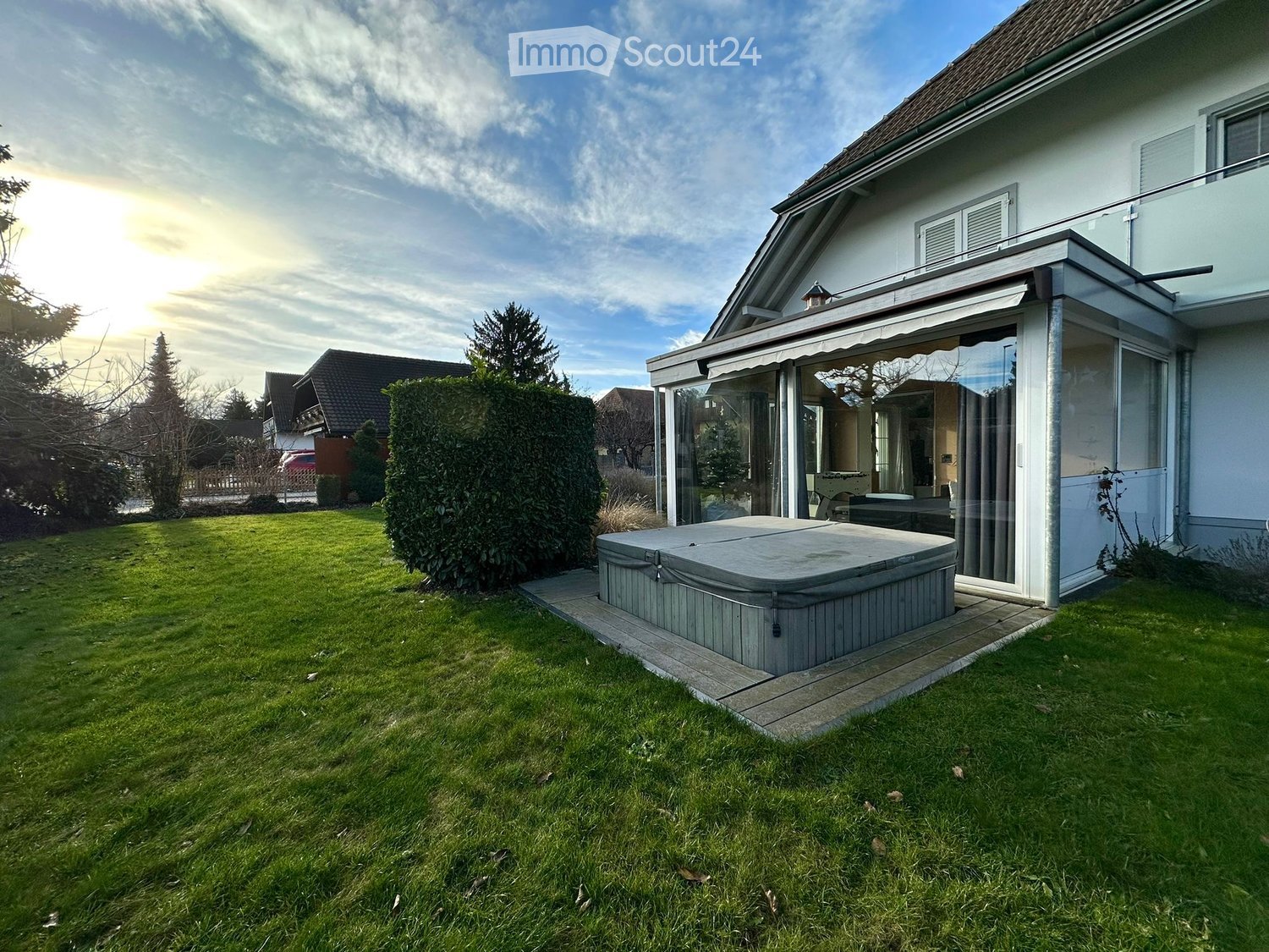 Well-maintained garden with a hot tub, neatly trimmed hedges, and a modern house with a covered patio area.