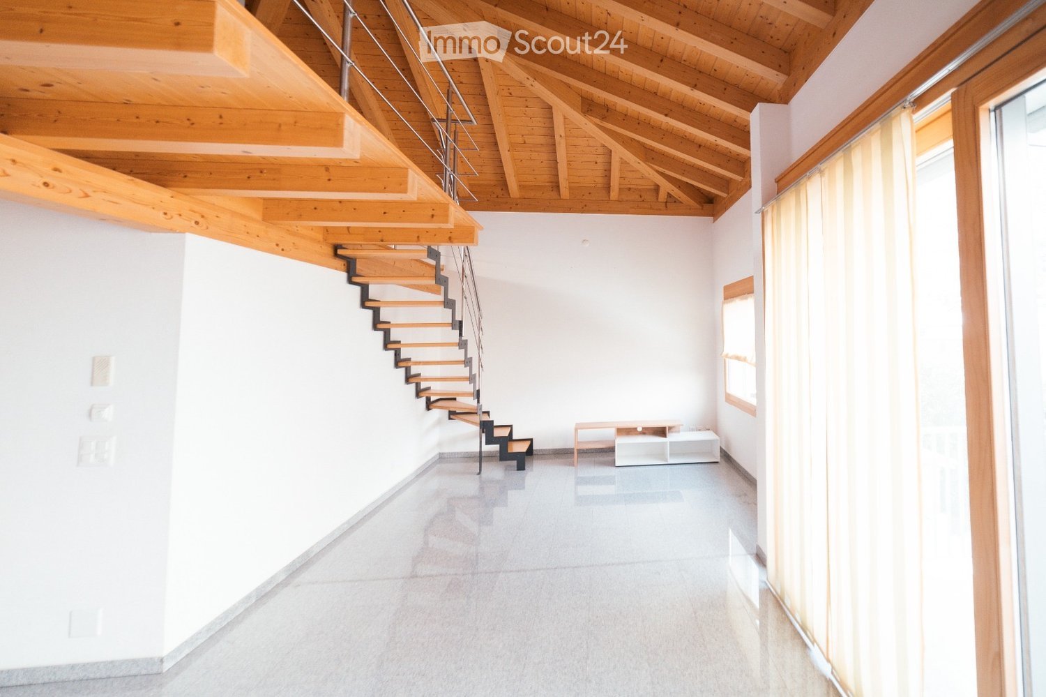 Modern hallway with exposed wooden beams, a sleek wooden staircase, and large windows allowing natural light to fill the space.