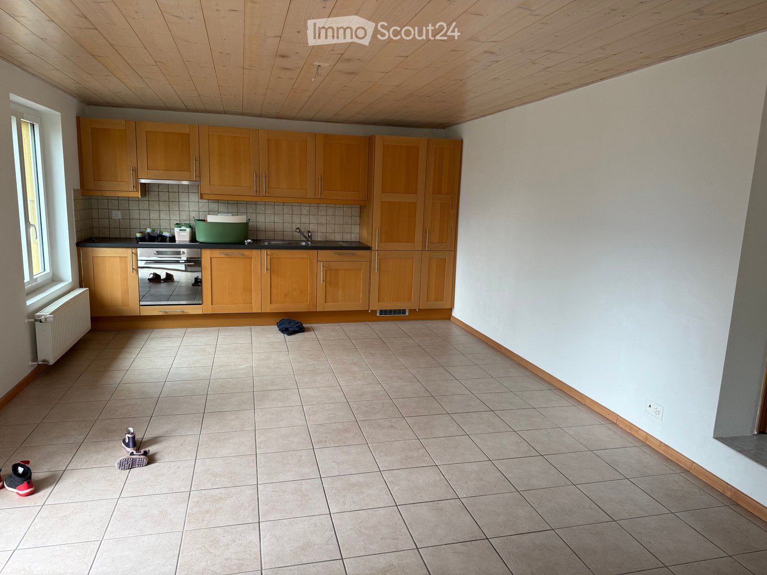 Empty kitchen with wooden cabinets, tiled floor, and a window. No furniture or appliances are present.