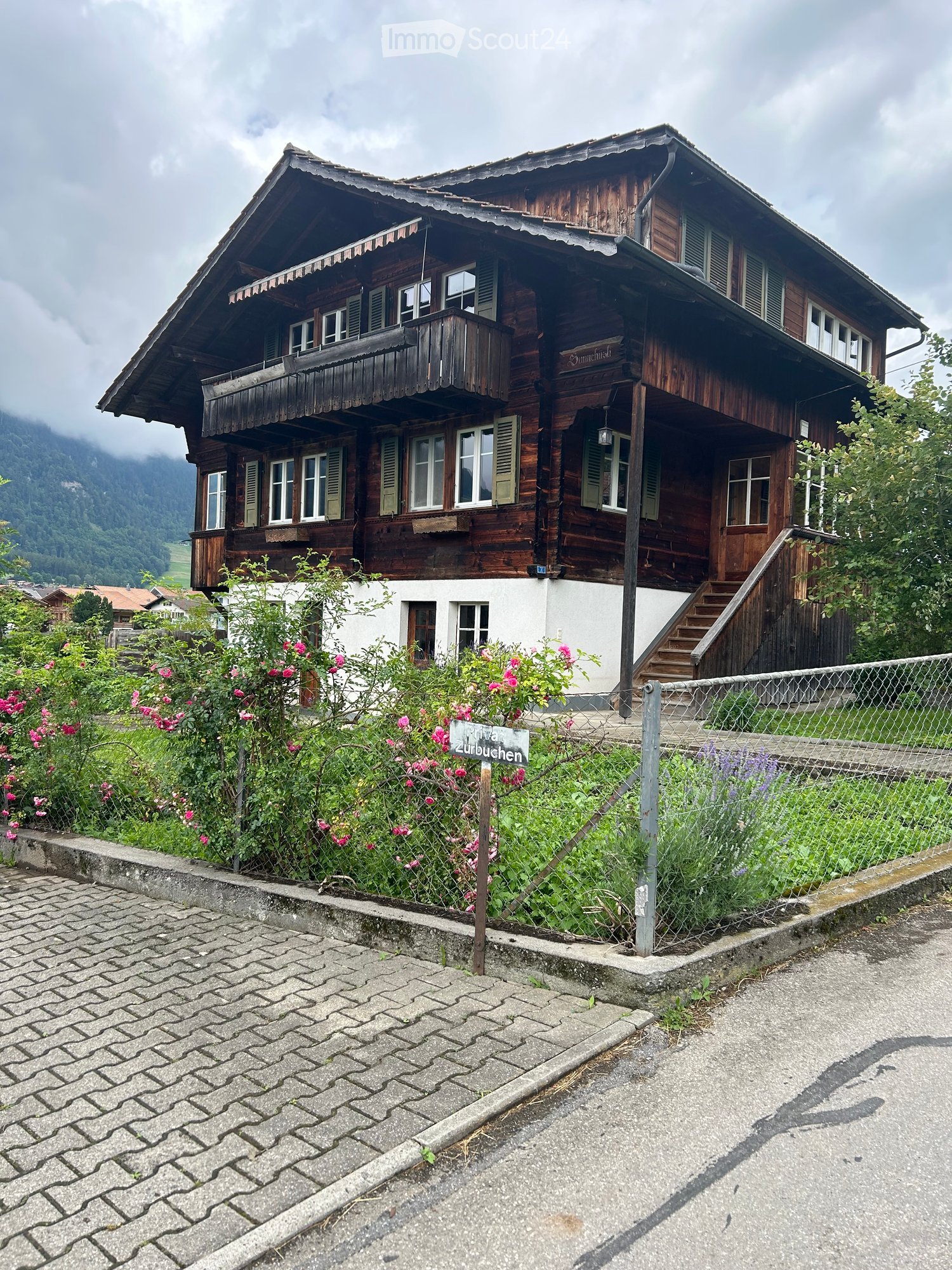 Traditional wooden house with a steep roof, multiple windows, and a balcony overlooking a scenic valley.