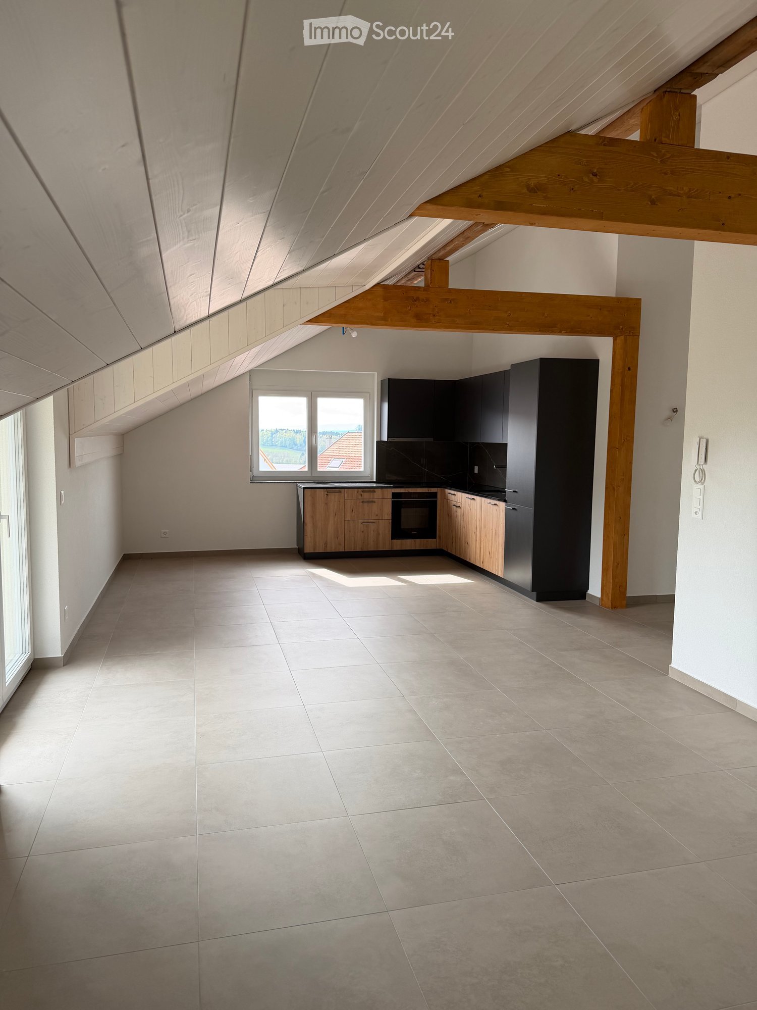 Modern kitchen with light wooden cabinets, black appliances, and large windows offering a view of the landscape.