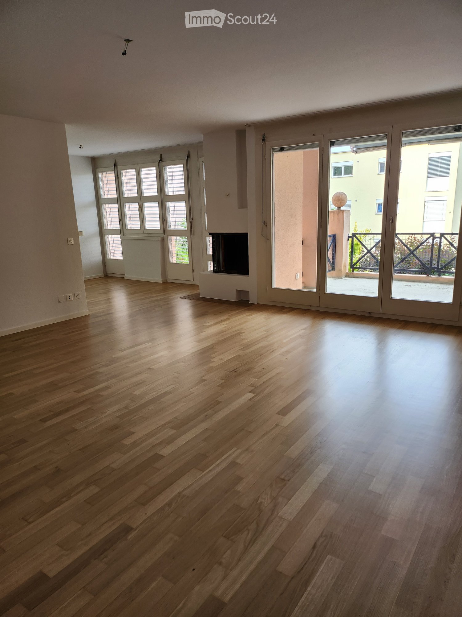 Empty room with wooden flooring, large sliding glass doors leading to a balcony, and a fireplace in the corner.