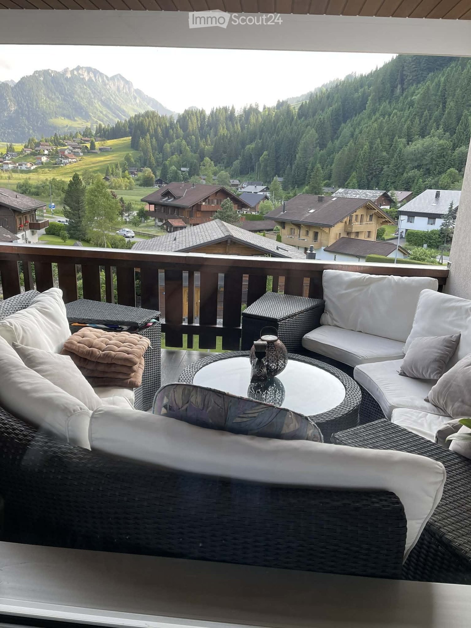 Balcony with wicker furniture, including a sofa, coffee table, and chairs, overlooking a scenic mountain landscape.