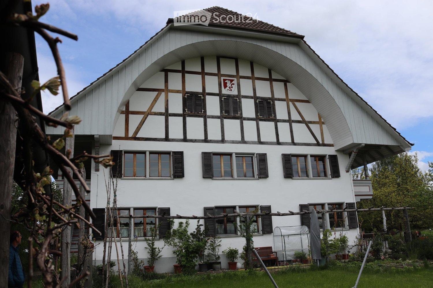 white house, red and white emblem, arched windows, sloped roof, black shutters, lush garden, potted plants, fence