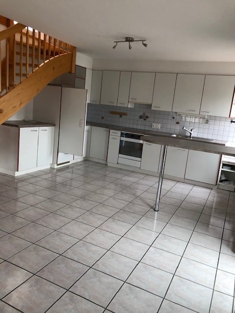Modern kitchen with white cabinets, tiled floor, central island, and built-in appliances including an oven and sink.