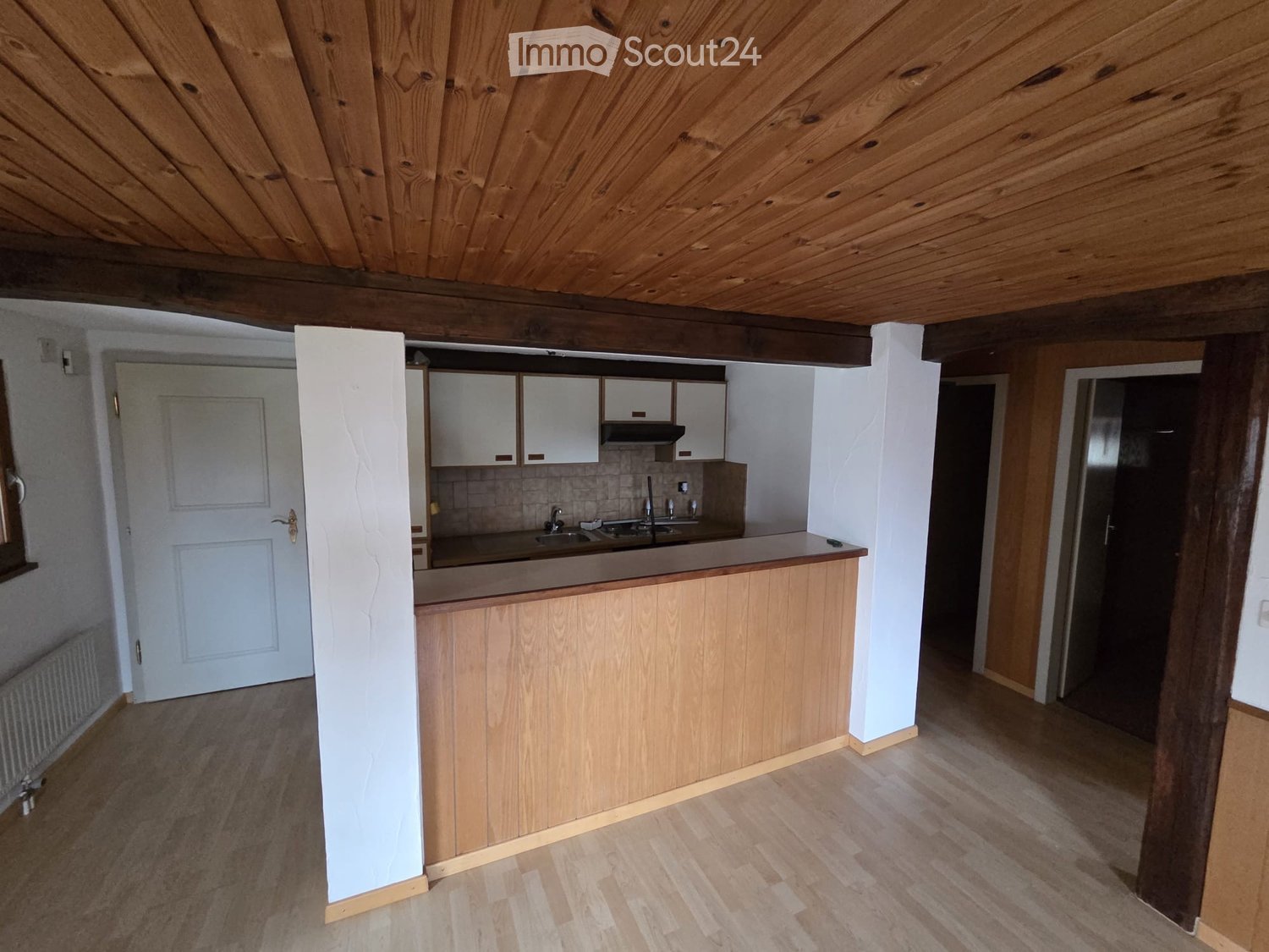 An empty kitchen with wooden countertop, sink with faucet, kitchen cabinets, wooden ceiling, and wooden flooring.