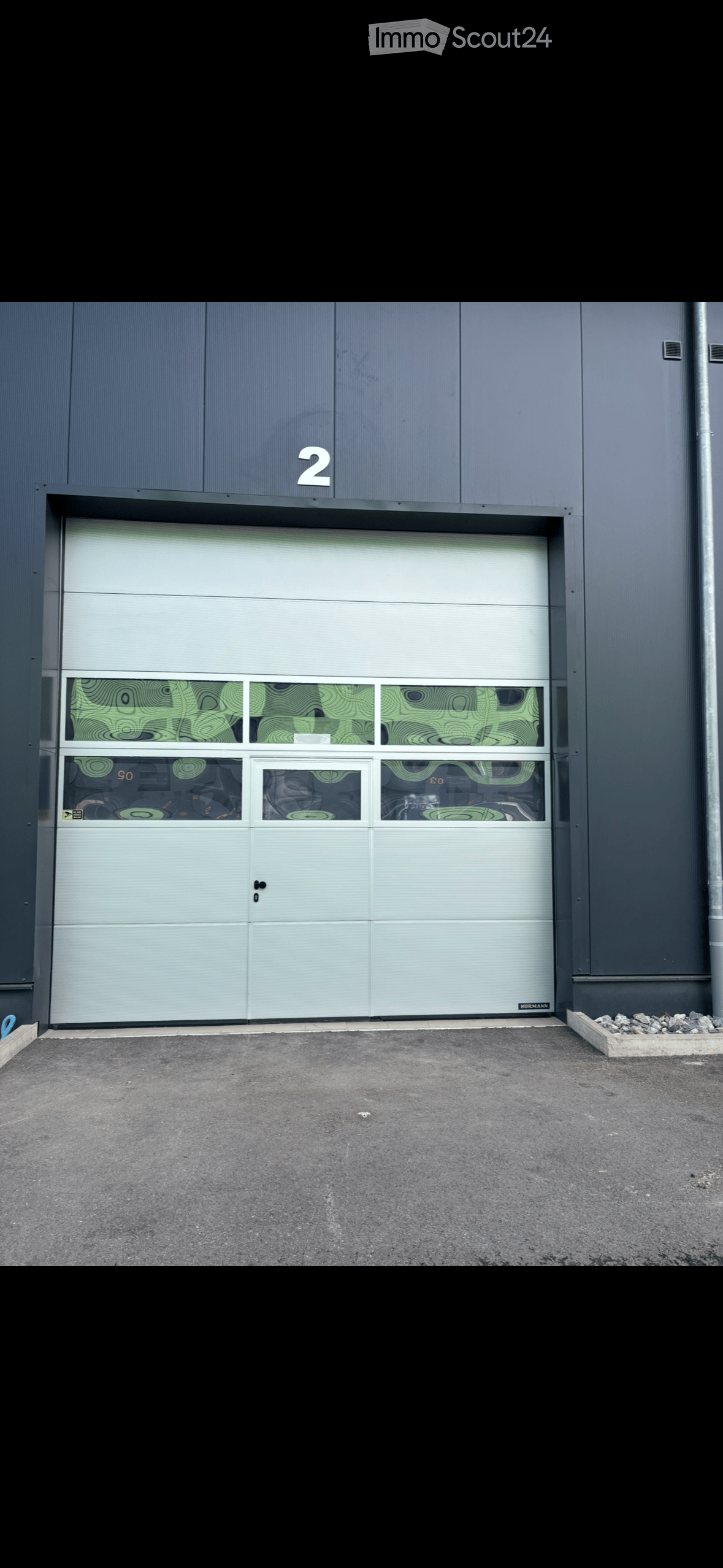 Modern building exterior with a large garage door featuring decorative glass panels and the number "2" above it.