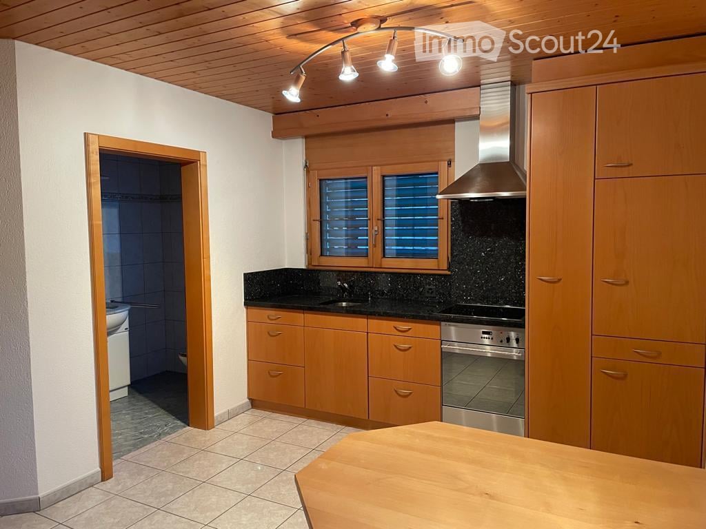 Bright kitchen with wooden cabinets, black granite countertops, stainless steel appliances, and a wooden island table. A bathroom is visible through an open doorway.