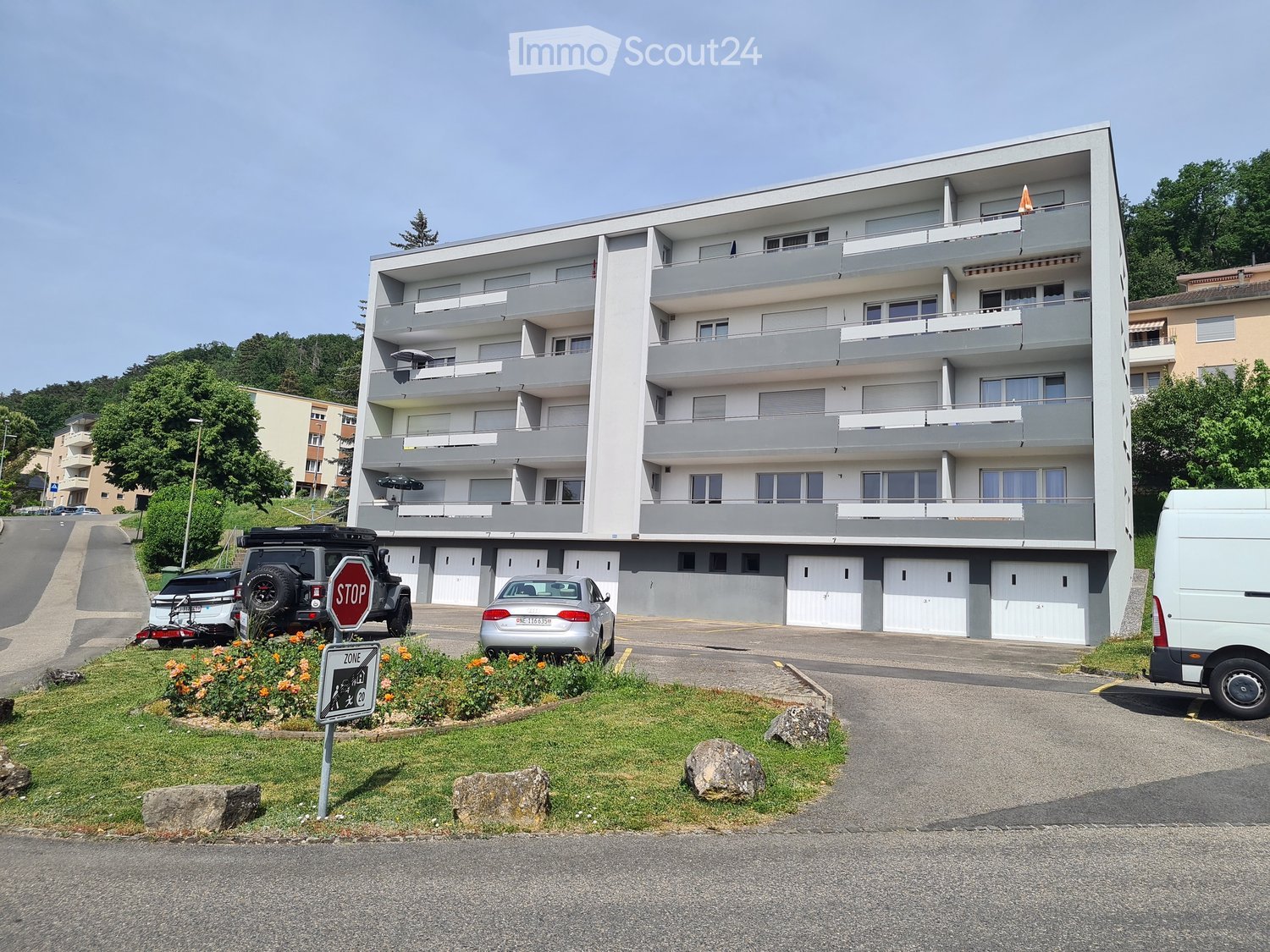 Modern multi-story apartment building with balconies, garage, and parking area.