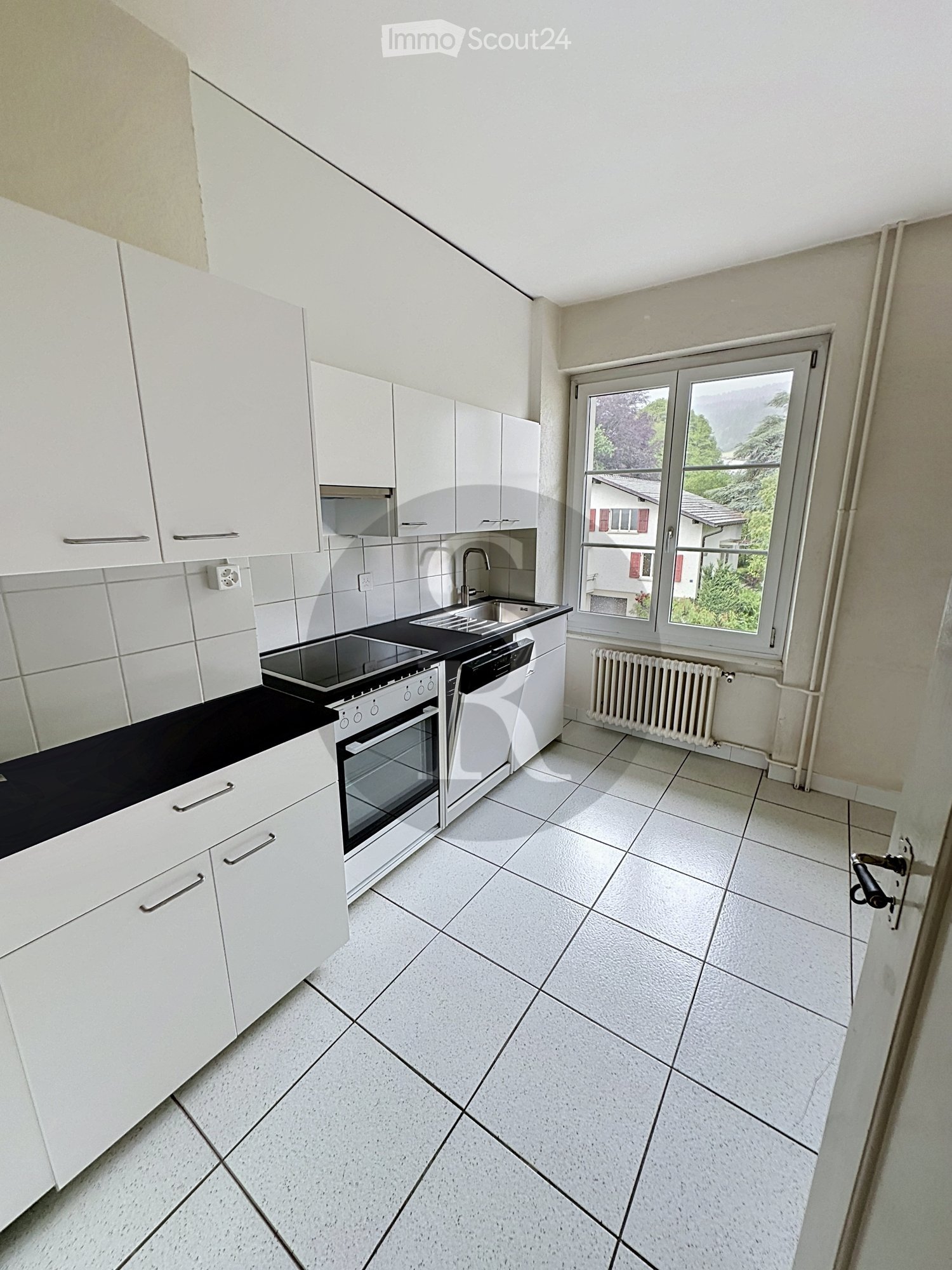 Modern kitchen with white cabinets, black countertop, tiled floor, and large window overlooking greenery.