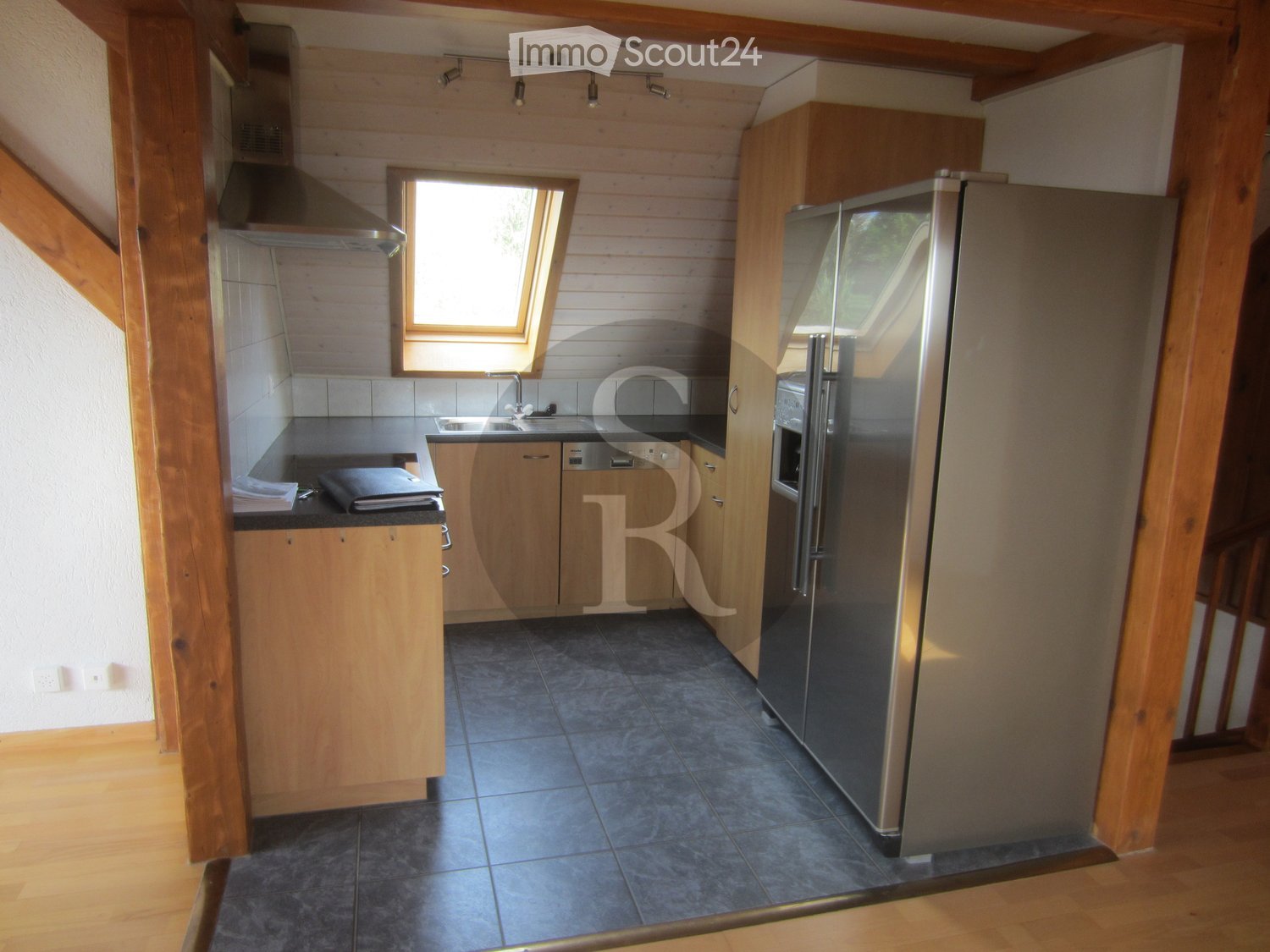Modern kitchen with wooden cabinets, stainless steel appliances, and a tiled floor. Features a refrigerator, sink, and range hood.