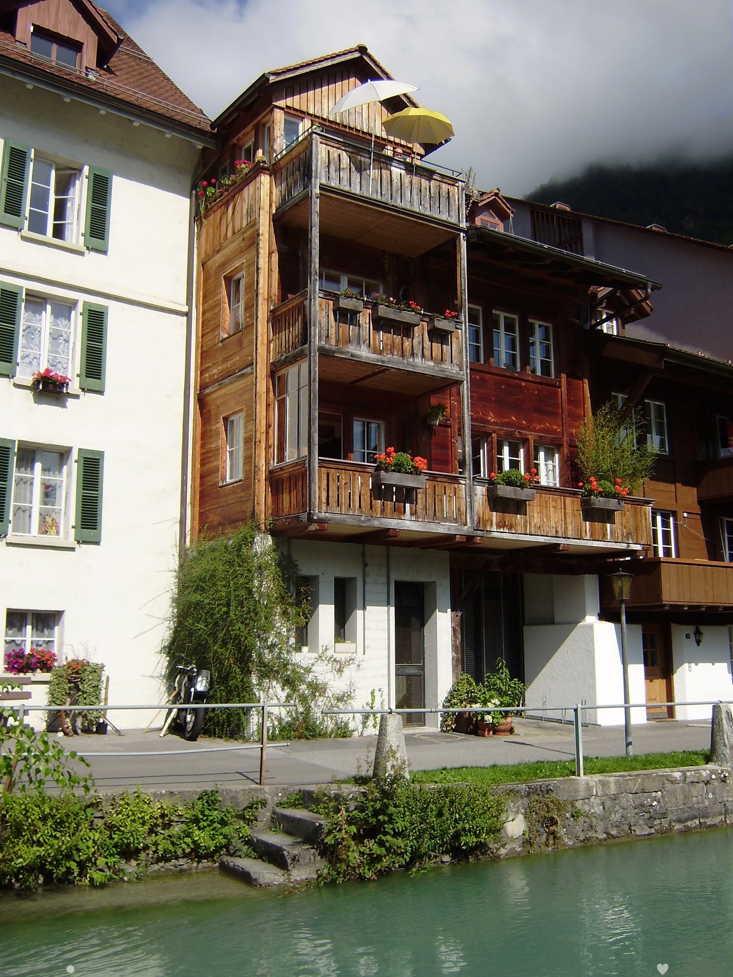 Multi-story wooden building with balconies, flower boxes, and shutters, situated near a canal.