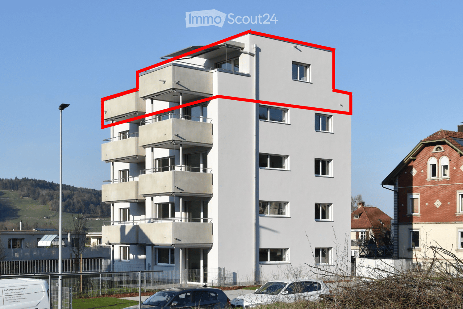Building. Modern multi-story residential building with balconies and large windows, surrounded by other structures and parked cars.