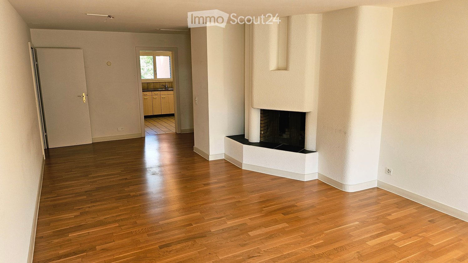 Spacious living room with polished hardwood floors, a built-in fireplace, and an open doorway leading to a kitchen area.