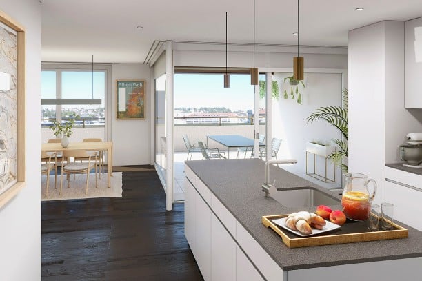Open-plan kitchen and dining area with modern white cabinets, dark countertops, pendant lights, and a view of the water. The dining area features a light wood table and chairs, and a potted plant is placed near the window.