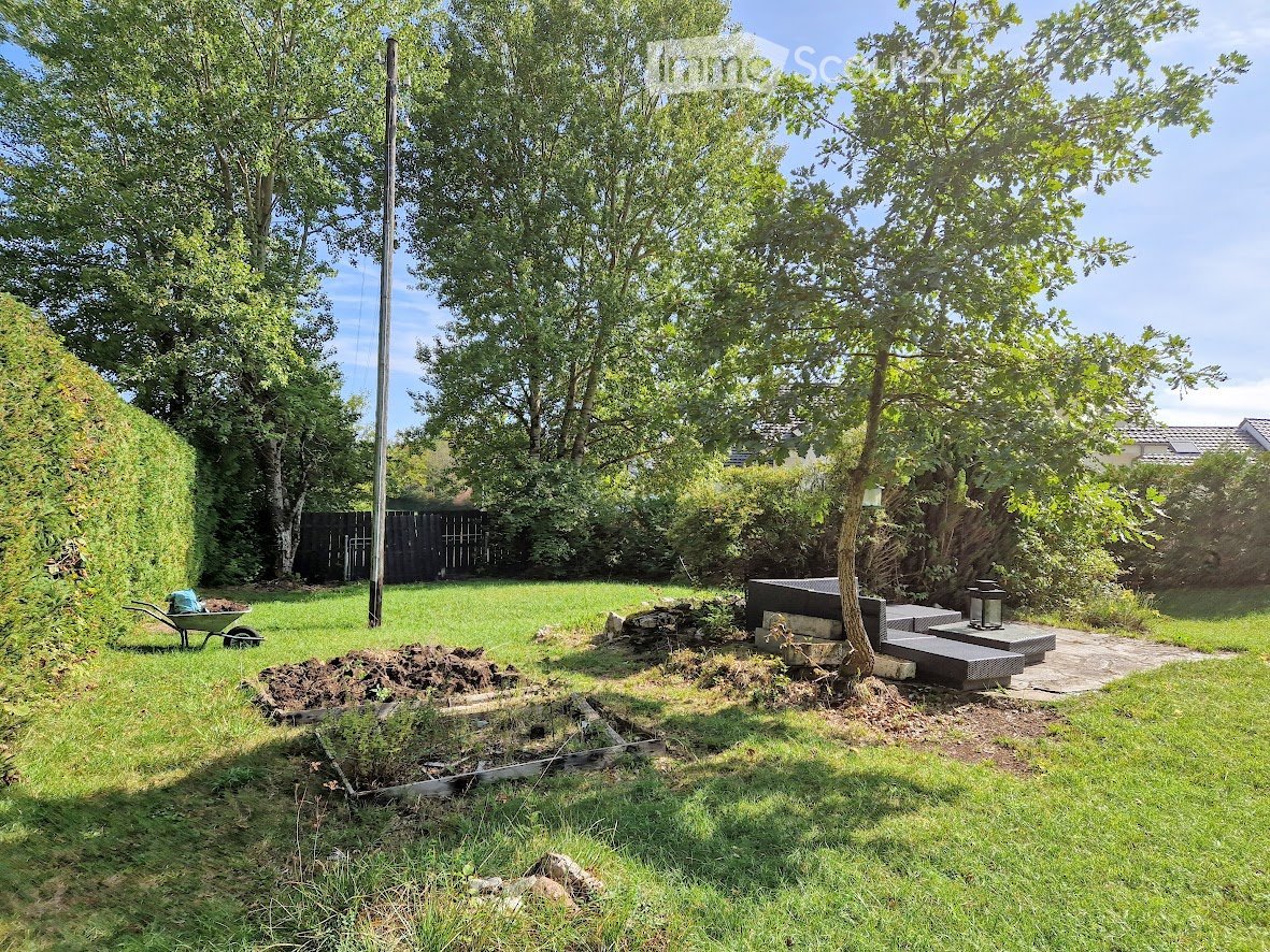 Well-maintained garden with a lawn, a tree, a wheelbarrow, a small stone seating area, and a wooden fence.