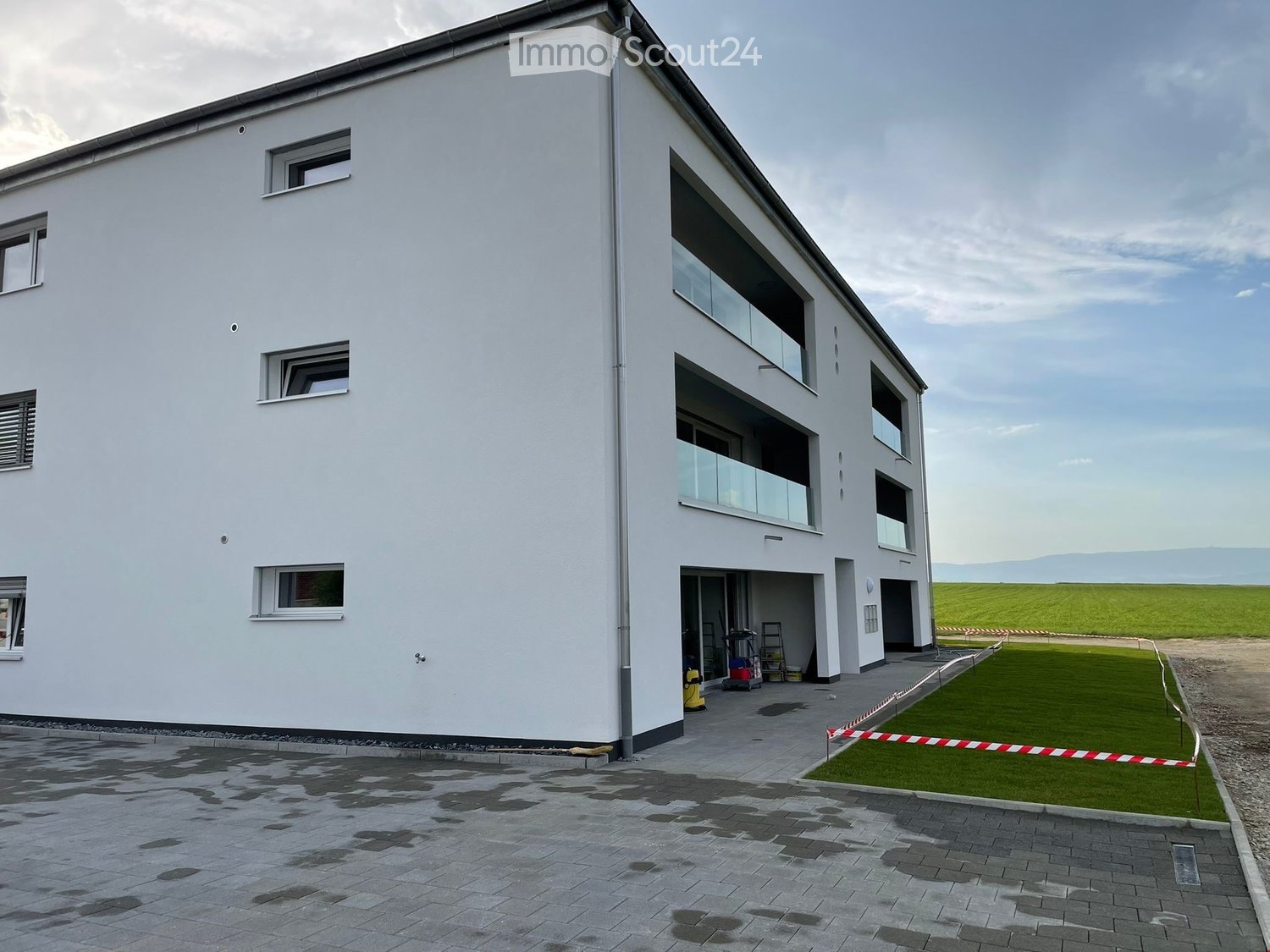 {"visible_features": ["Parking place"],"type": "Commercial building","description": "3-story commercial building with a modern, minimalist design. The building has large windows, a flat roof, and a paved parking area in front. The surrounding area appea