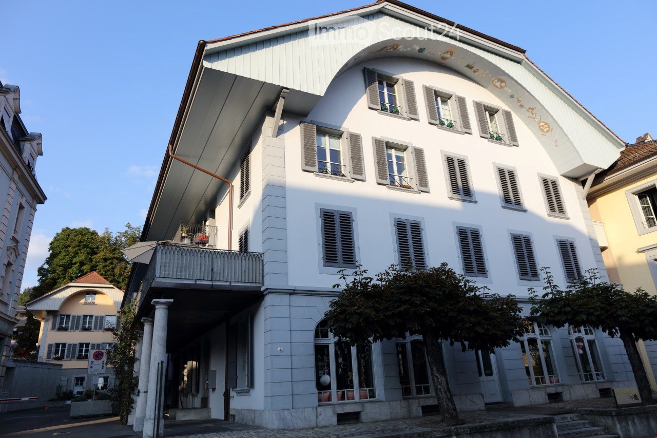A multi-story white building with a curved roof, multiple windows with shutters, and a balcony on the second floor.