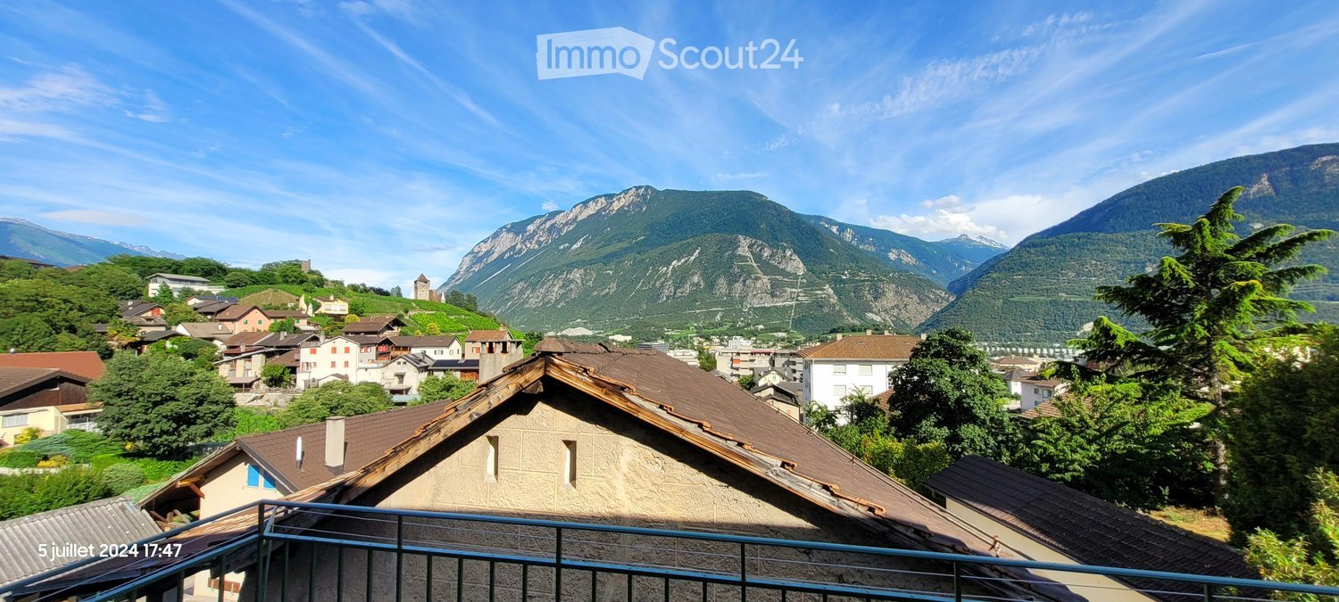 Balcony overlooking a picturesque village with traditional houses and a backdrop of mountain ranges.