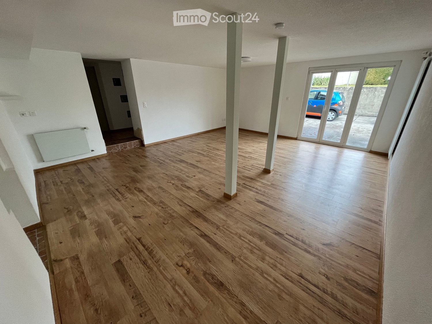 Empty room with wooden flooring, white walls, and a large sliding glass door leading to an outdoor area.