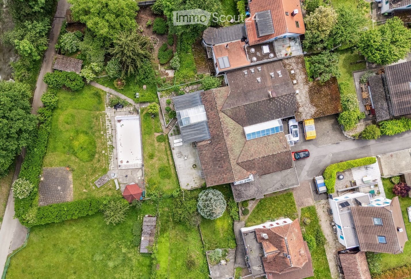 Aerial view of a residential neighborhood with multiple houses, gardens, driveways, and parked cars.
