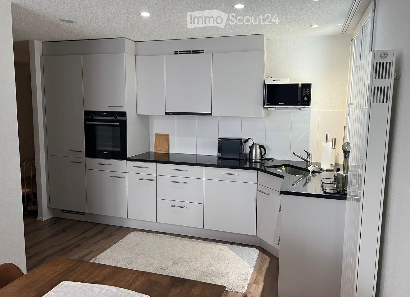 Modern kitchen with white cabinets, black countertops, and stainless steel appliances including an oven, microwave, toaster, and sink.