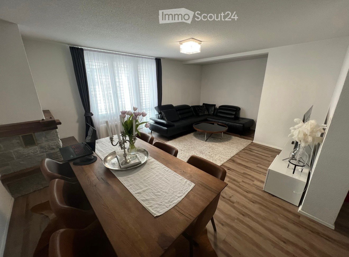 Furnished Room. Modern living and dining area with a black leather sofa, coffee table, dining table with chairs, laptop, and decorative items.