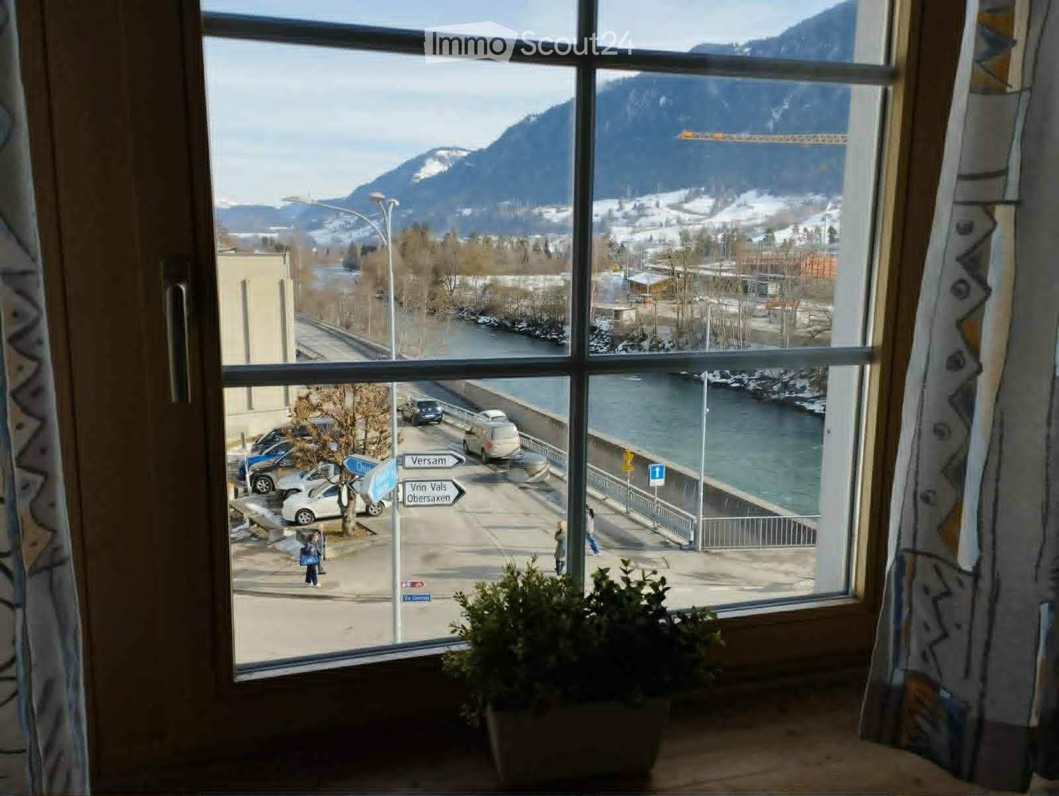View from a window showing a river, mountains, and a road with street signs and parked cars.