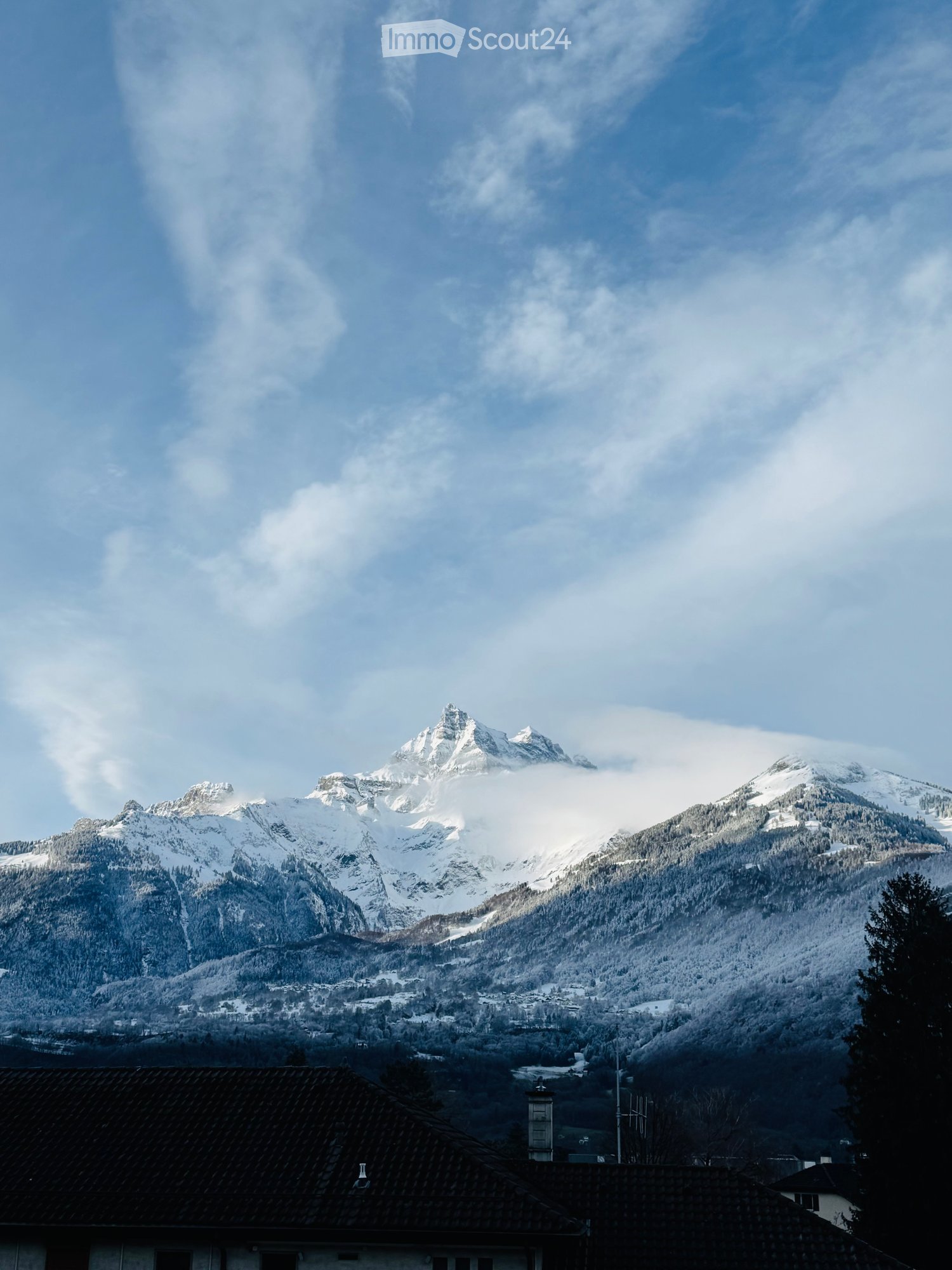 A view of a snow-covered mountain range with a small house in the foreground.