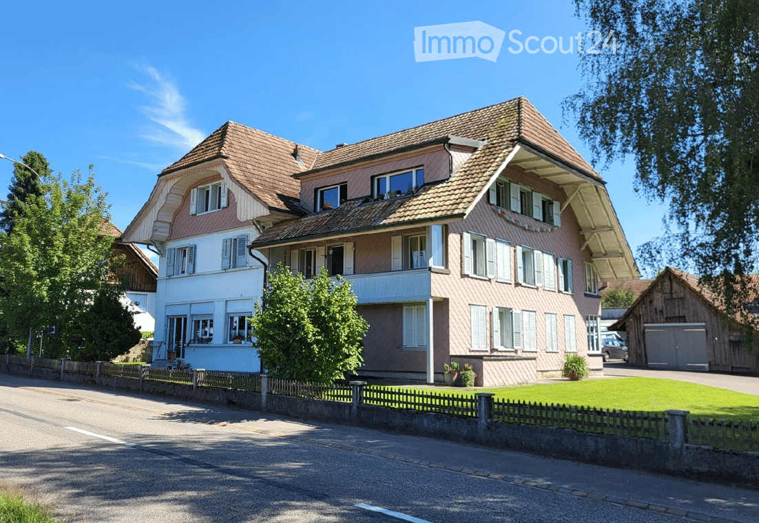Large house with brown roof, two stories, windows with white shutters, front yard, balcony