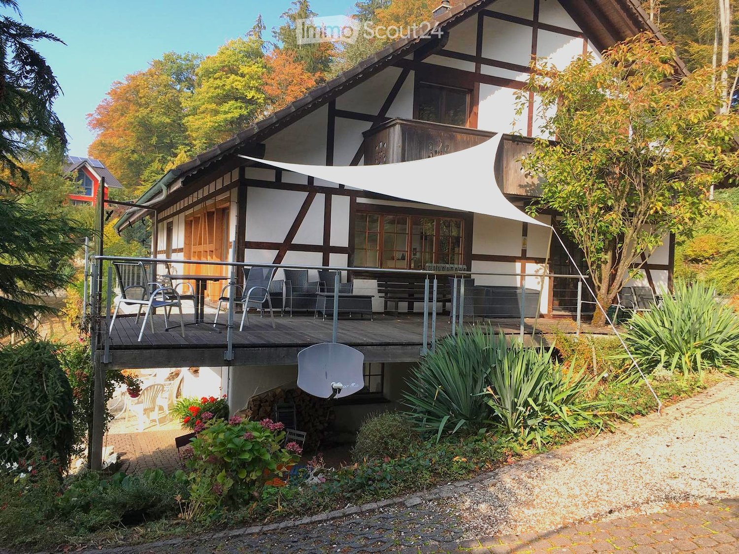 Traditional half-timbered house with a spacious wooden balcony, outdoor furniture, and surrounding garden area.