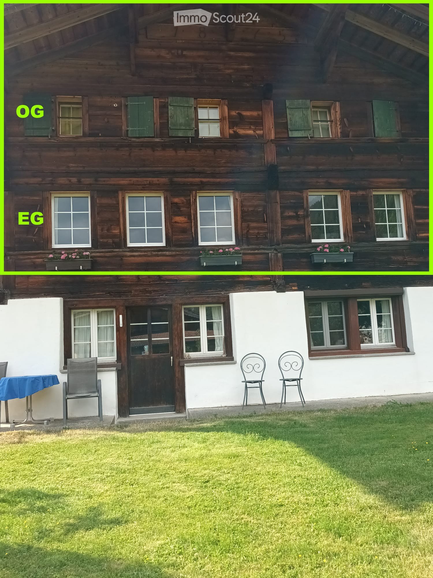 Two-story wooden house with green shutters, multiple windows, and a small garden area with chairs and a table.