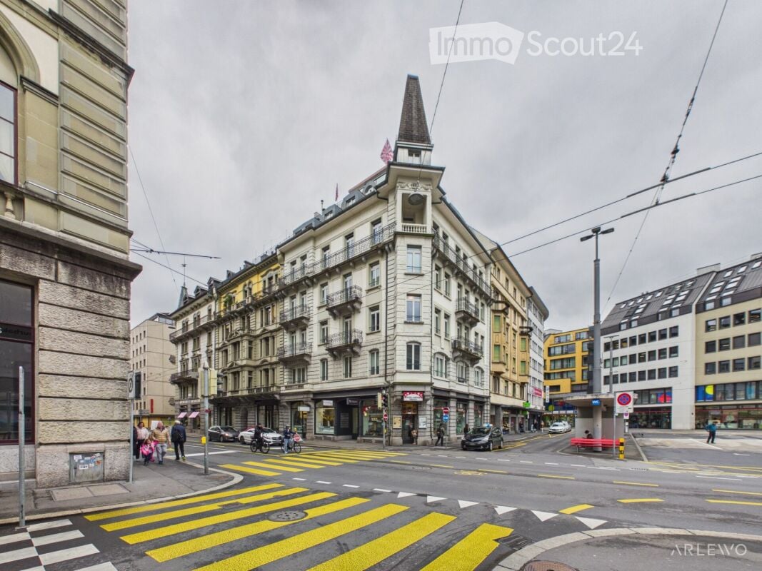 A multi-story building with a distinctive tower and spire, located at a street corner with a pedestrian crossing.