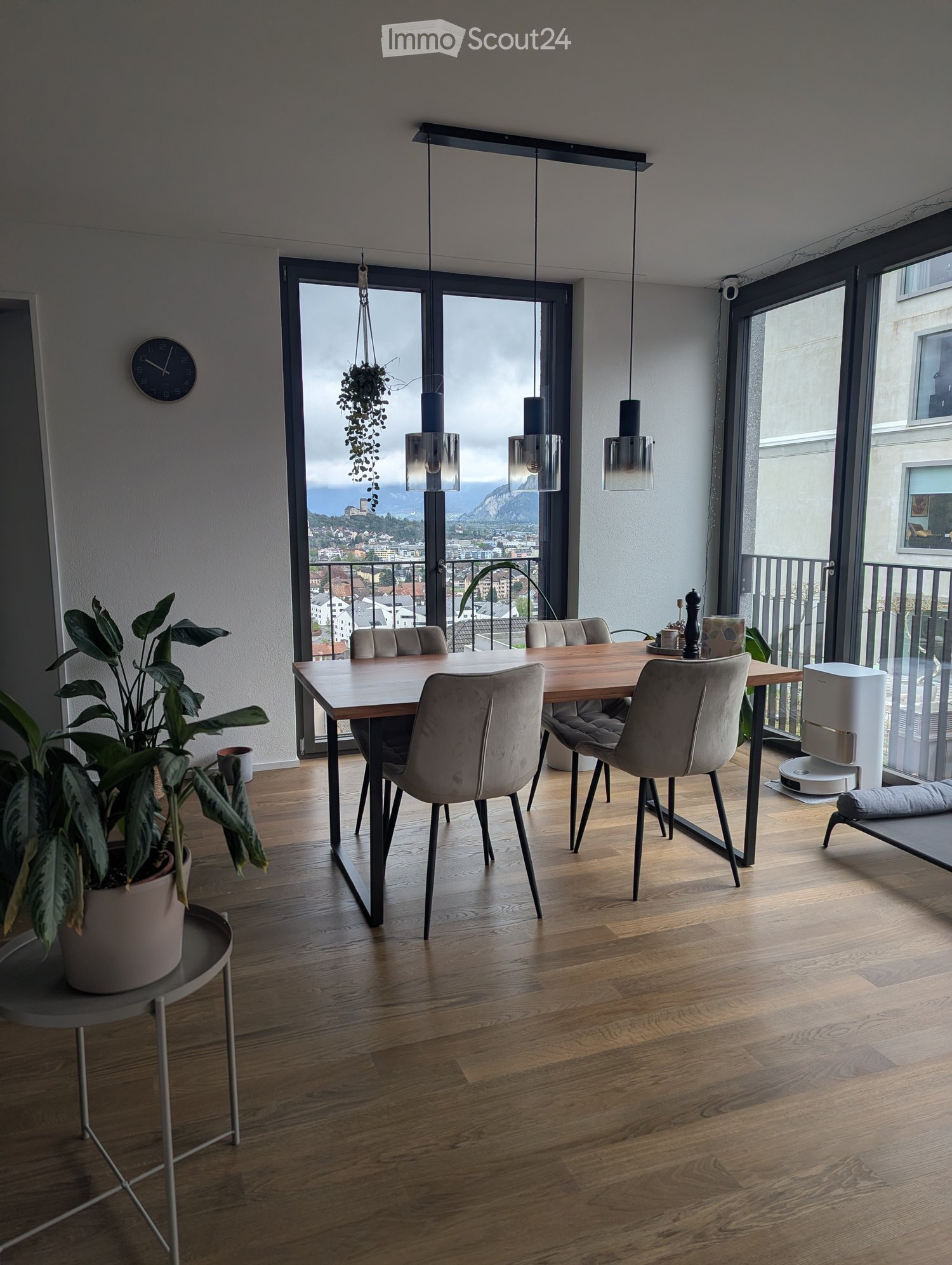Modern dining area with wooden floor, large window offering a scenic view, dining table with chairs, potted plants, and modern lighting.