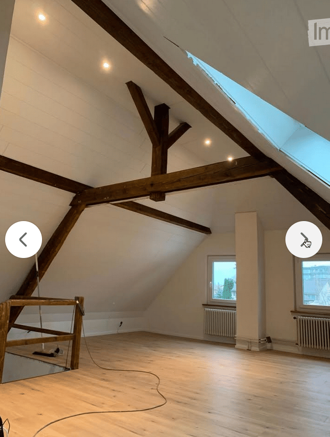 Empty attic space with wooden beams, skylight, wooden flooring, and white walls. No furniture or equipment present.