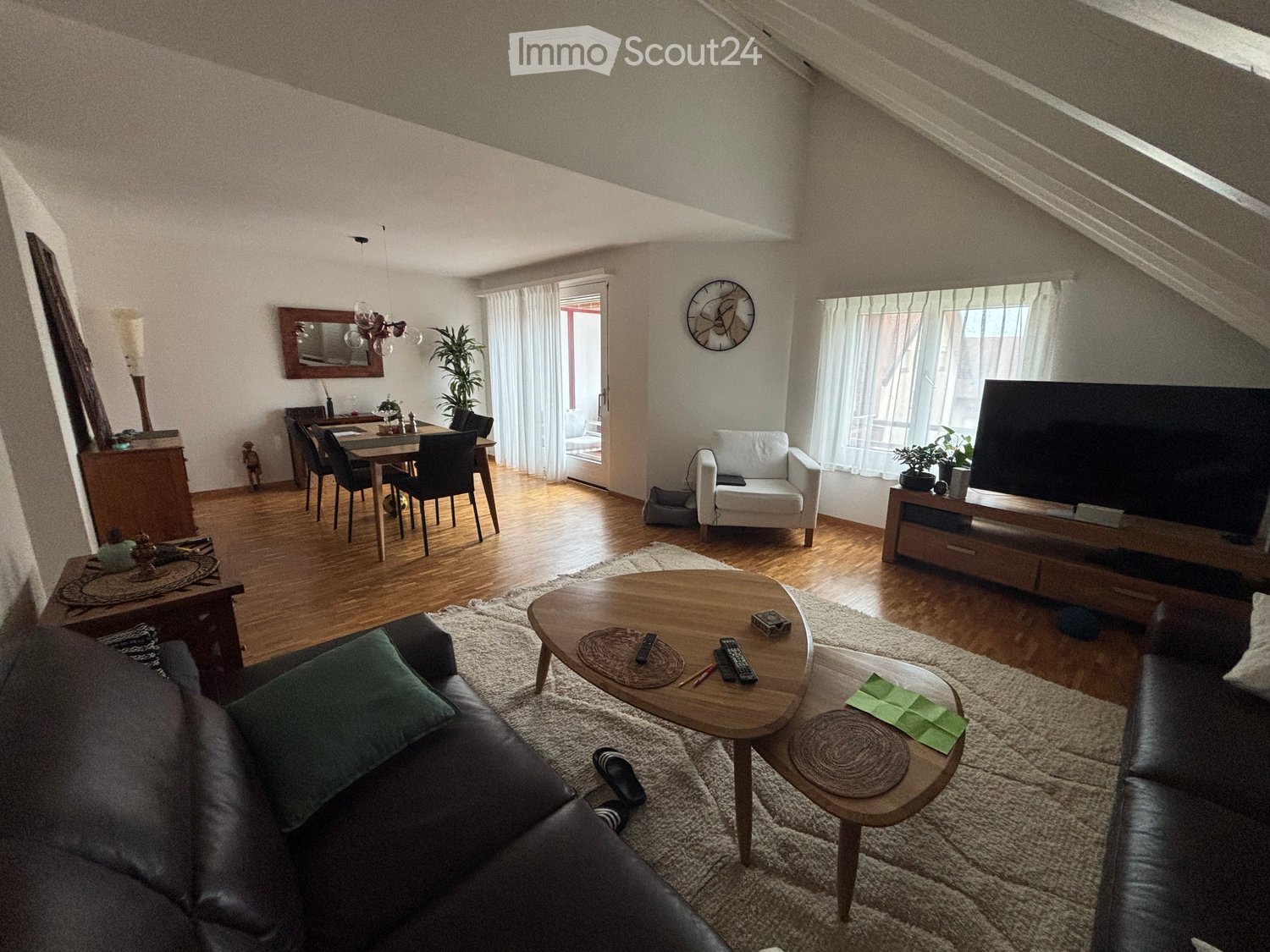 Living room with wooden flooring, a sofa, coffee table, dining area, TV, and decorative items.
