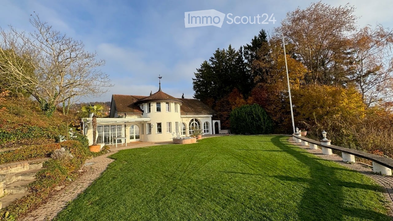 A well-maintained garden with a circular lawn, a modern house with large windows and a dome-shaped roof, and a paved pathway leading to the house.
