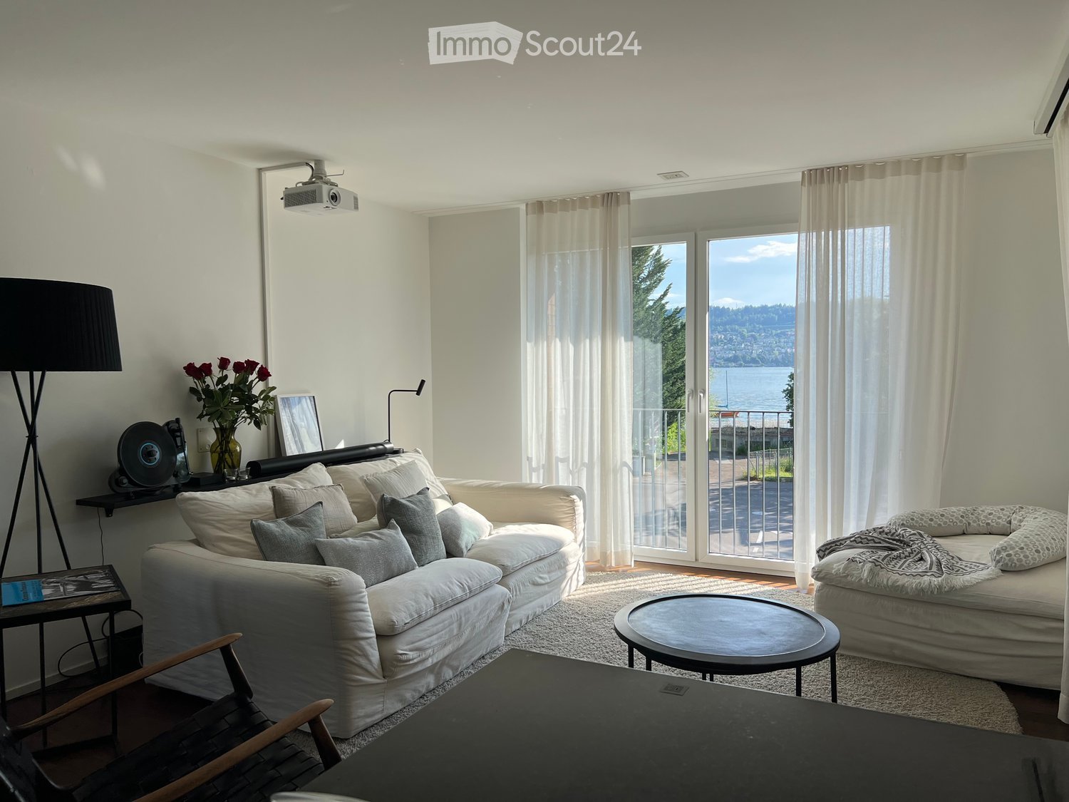 Bright living room with large windows and a view, featuring a white sofa, coffee table, side table, and decorative items.
