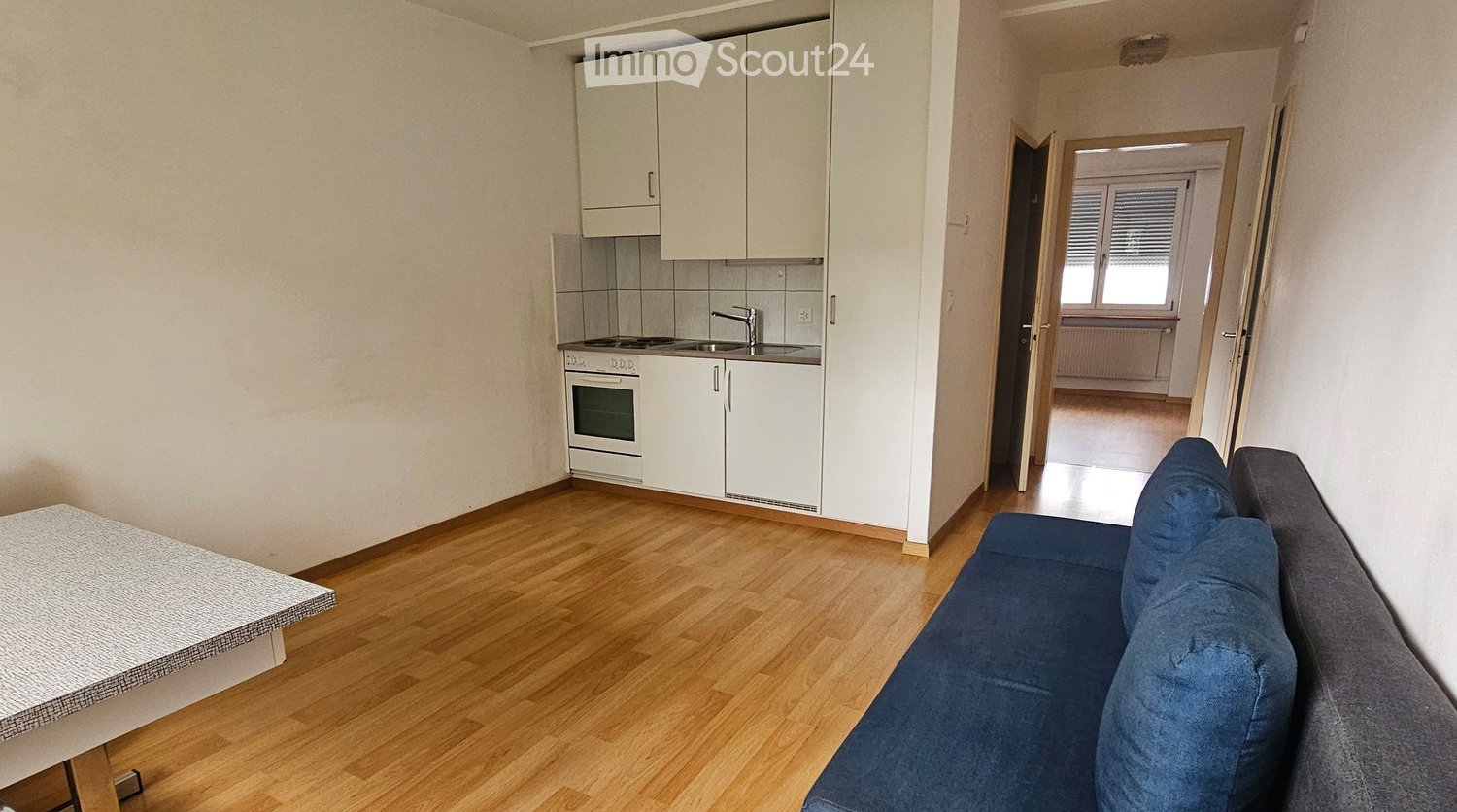 A modern, furnished living space with a sofa, a small table, and an adjacent kitchen area featuring white cabinets, an oven, and a sink.